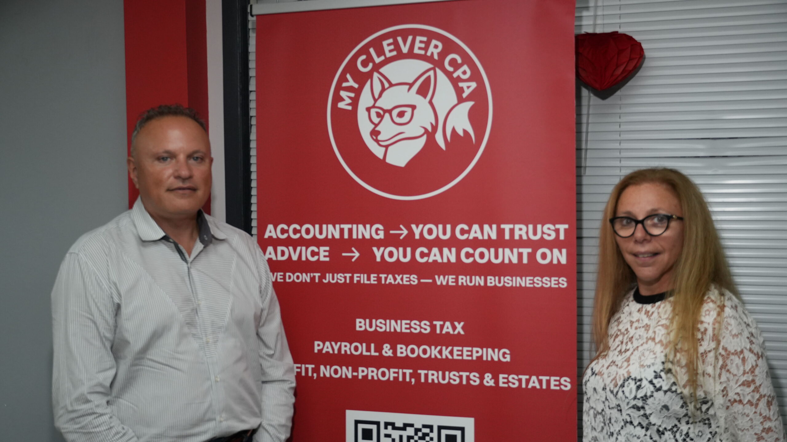 Two members of the MyCleverCPA team standing beside the firm's banner